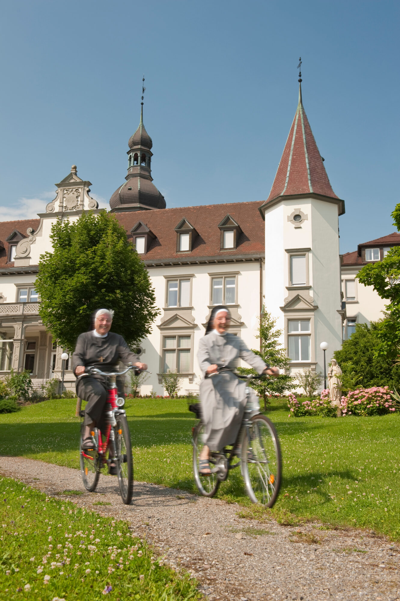 Zwei Kreuzschwestern auf dem Fahrrad vor der Hegner Klosteranlage