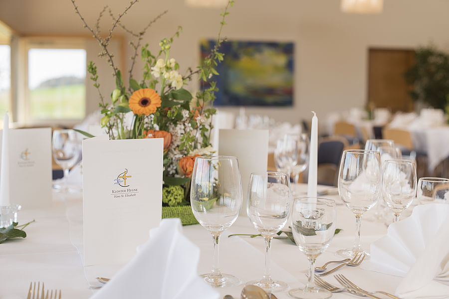 mit weißer Tischdecke, Servietten, Weingläsern und einem Blumenstrauß gedeckter Tisch